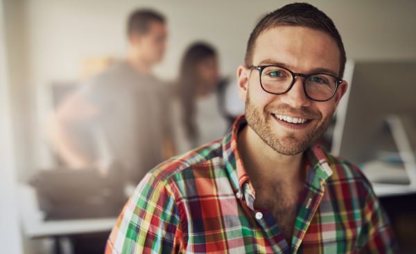 Cheerful entrepreneur wearing glasses in the office Attraktiver junger Herr in kariertem Hemd, lachend in die Kamera.