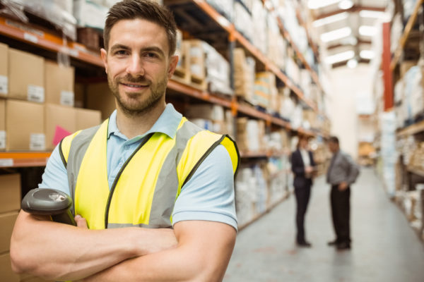 echtes-unechtes-factoring-2 Lächelnder Arbeiter mit verschränkten Armen im Lagerhaus.