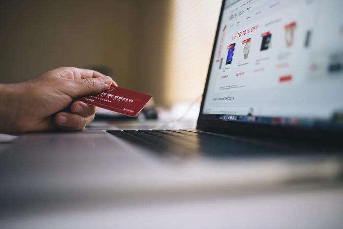 Firmenkreditkarte Person hält Kreditkarte in der Hand und Laptop steht auf dem Tisch