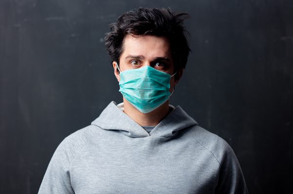 young white man in protective mask on dark background